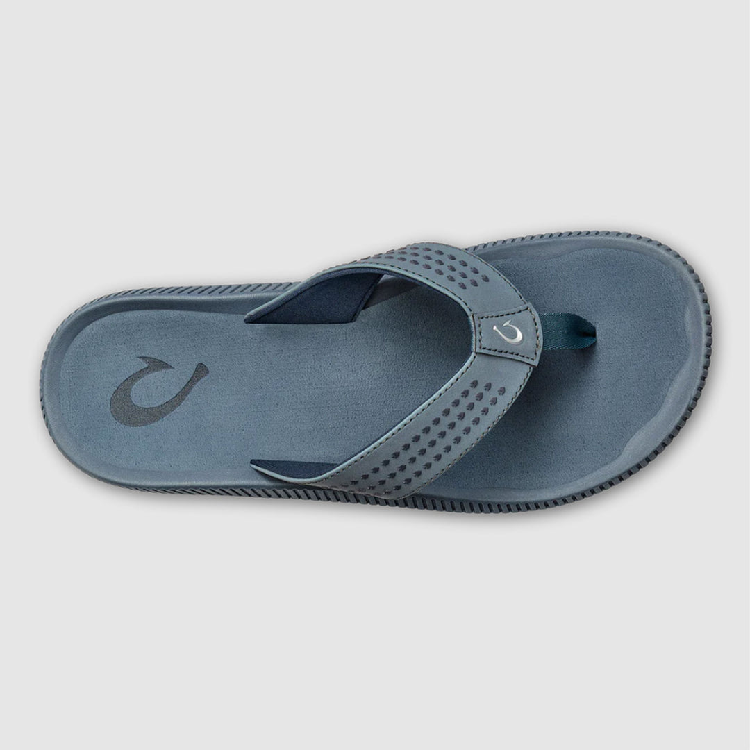 A single slip-on thong sandal shown from a top-down view on a light gray background. The sandal has a muted blue-gray footbed and strap with a perforated pattern on the strap, a dark gray logo on the footbed, and a dark teal toe loop.